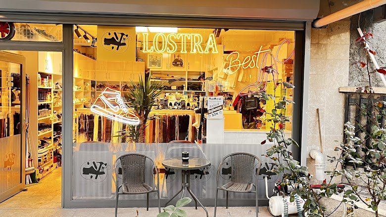Ayakkabı Yenileme Servisi atölyesinin vitrini, Öveçler: neon LOSTRA tabelası ve sneaker logosu, önünde iki sandalye ve masa